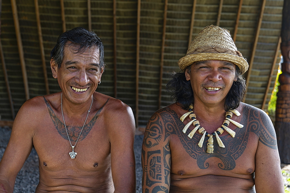 Two men with tattoos - one with a chain made from carved whale bones - smile at the camera in the Te Tumu cultural center, Tekoapa, Ua Huka, Marquesas Islands, French Polynesia, South Pacific