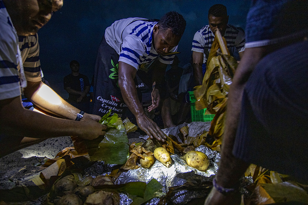 The Lovo underground furnace opens to passengers of cruise ship MV Reef Endeavor (Captain Cook Cruises Fiji) during a nightly village visit, Gunu, Naviti Island, Yasawa Group, Fiji Islands, South Pacific