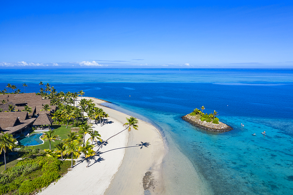 Aerial view of a Residence Villa accommodation in the Six Senses Fiji Resort with coconut trees, a beach and a family enjoying water sports activities next to a small offshore island, Malolo Island, Mamanuca Group, Fiji Islands, South Pacific