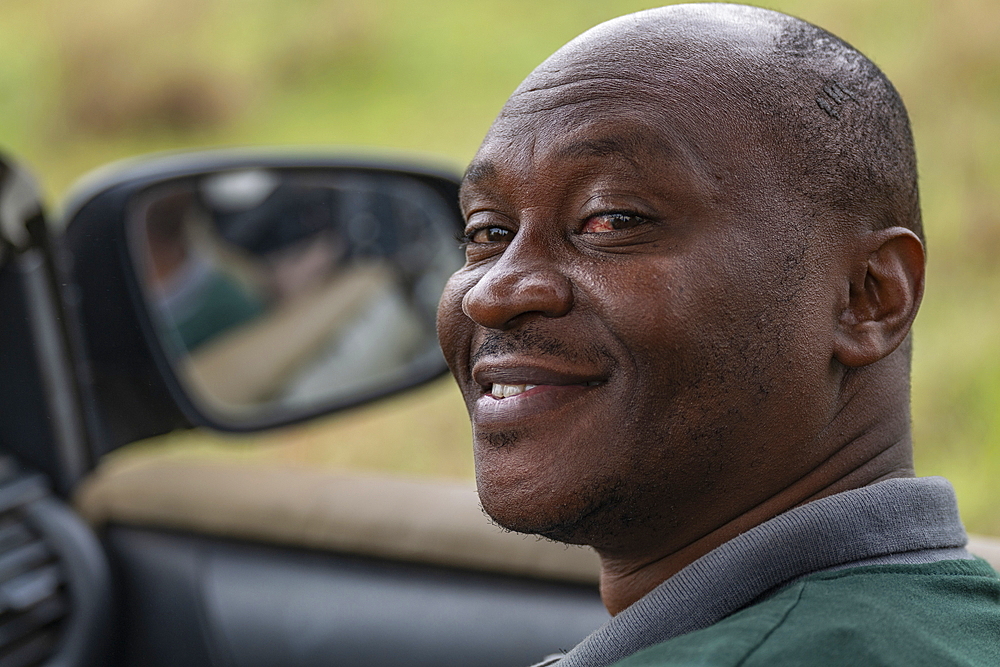 Portrait of a smiling Rwandan man in a safari vehicle operated by luxury resort tented Magashi Camp (Wilderness Safaris), Akagera National Park, Eastern Province, Rwanda, Africa