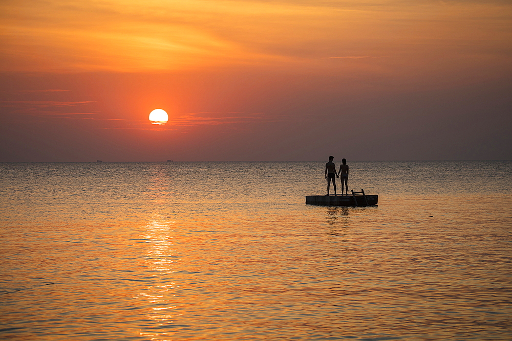 Silhouette of a young couple standing on a bathing platform in front of Ong Lang Beach at sunset, Ong Lang, Phu Quoc Island, Kien Giang, Vietnam, Asia