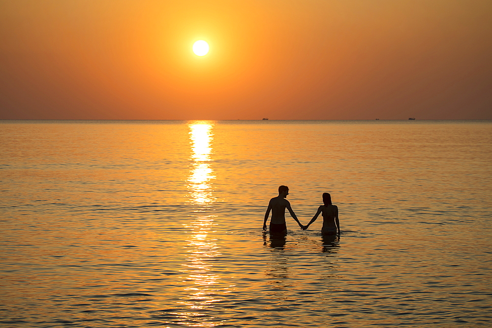 Silhouette of a romantic young couple holding hands in the water in front of Ong Lang Beach at sunset, Ong Lang, Phu Quoc Island, Kien Giang, Vietnam, Asia