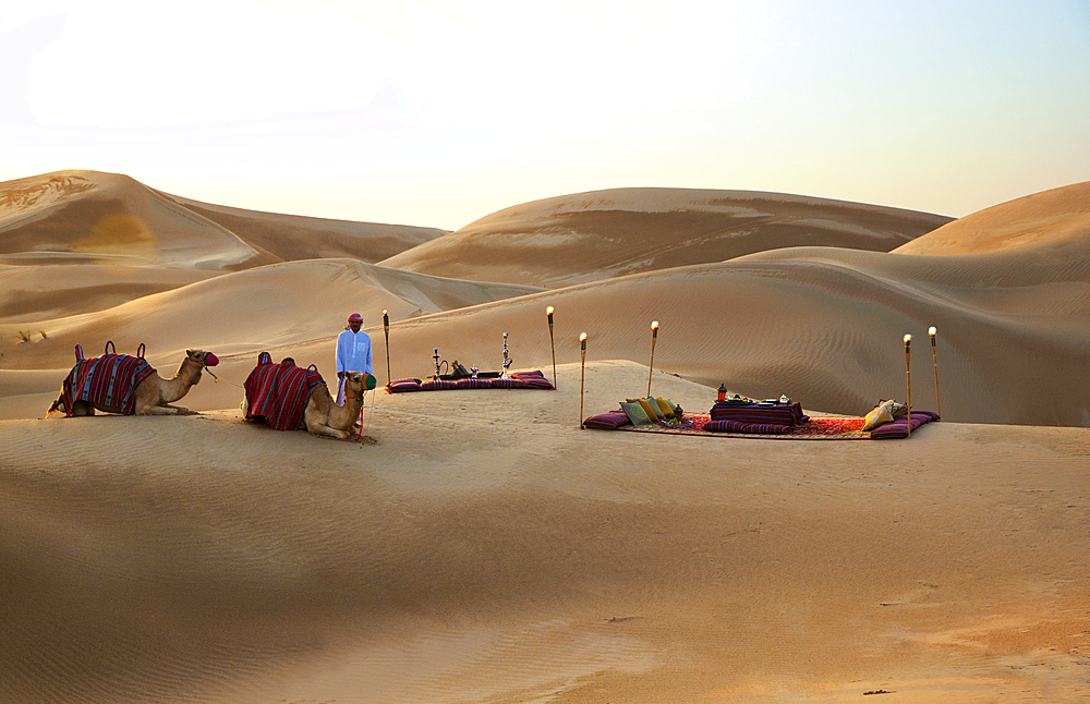 A beautiful desert picninc, set amidst the sanddunes, with a couple of camels and their minder in the foreground. Shot in Saudi Arabia.