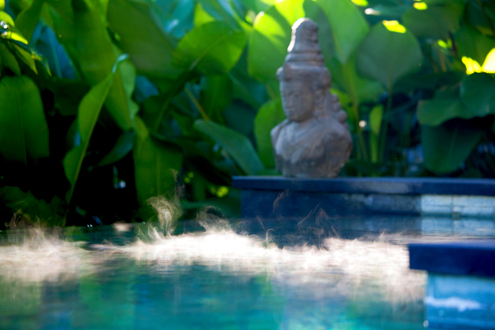 Morning steaam on the surface of a pool with a Hindu statue on the side. Shot in a propical setting. Bali, Indonesia