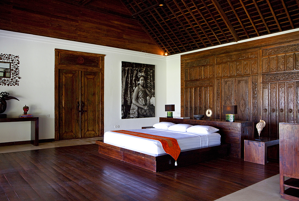 An interior shot of a Bali bedroom, designed and built in hardwood, with a carved door used as a headboard.