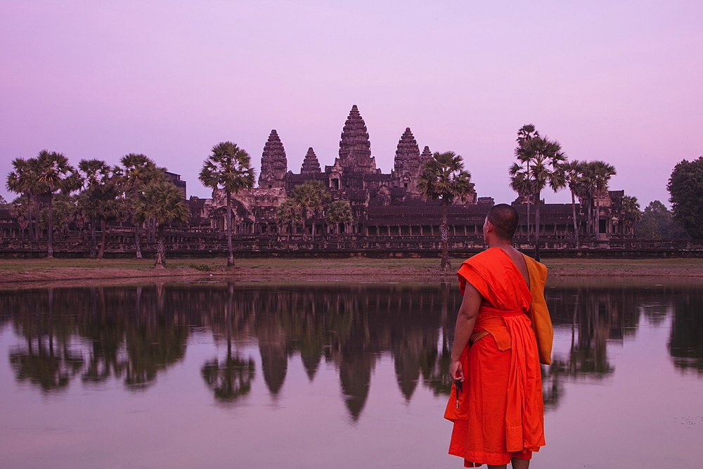 Buddhist monk stands by the moat and admires Angkor Wat temple at sunset, Angkor Wat, near Siem Reap, Siem Reap Province, Cambodia, Asia