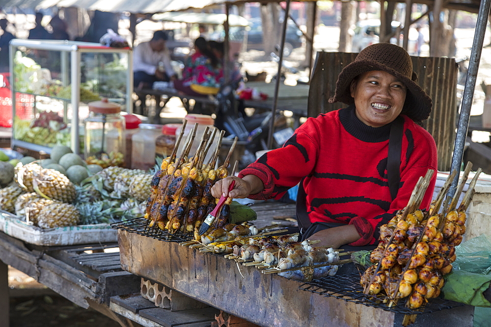 Happy woman with stuffed grilled frog at a street food stall in the market, Oudong (Udong), Kampong Speu, Cambodia, Asia