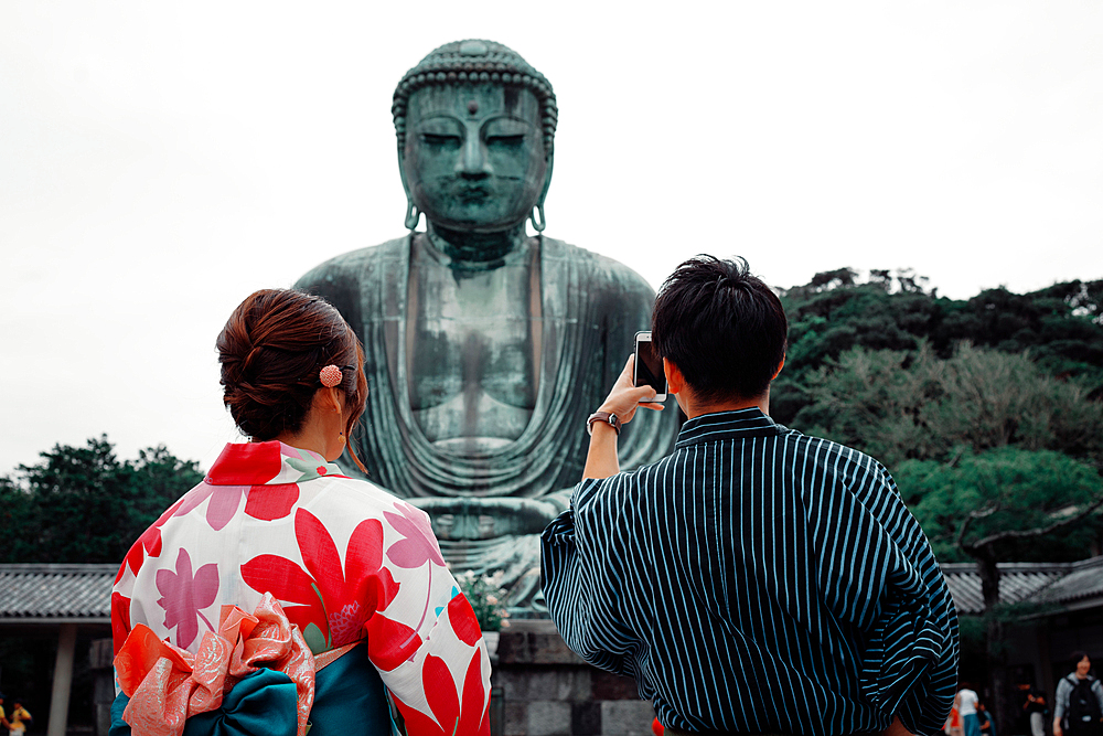 Koutokuin Temple with couple in foreground taking a photo of Buddha statue, Toyko, Japan