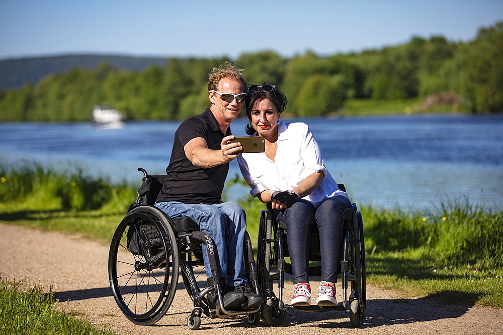 Couple in wheelchairs making selfie photo on the Main, Großwallstadt, Spessart-Mainland, Franconia, Bavaria, Germany, Europe