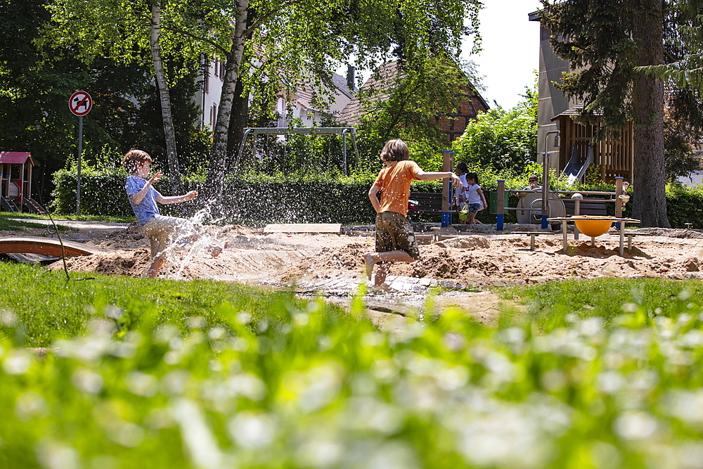 Two boys have fun and splash themselves with water on an urban playground, Tauberbischofsheim, Baden-Wuerttemberg, Germany, Europe