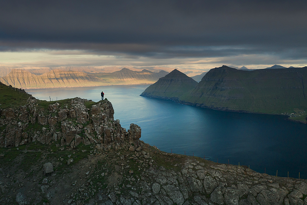 Hikers at Hvithamar near the town of Gjogv on the Faroe island of Eysturoy with a panoramic view of the fjord at sunset