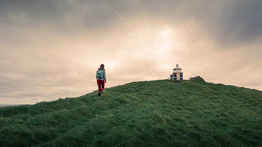 Woman hikes to lighthouse on Kalsoy Island, Faroe Islands