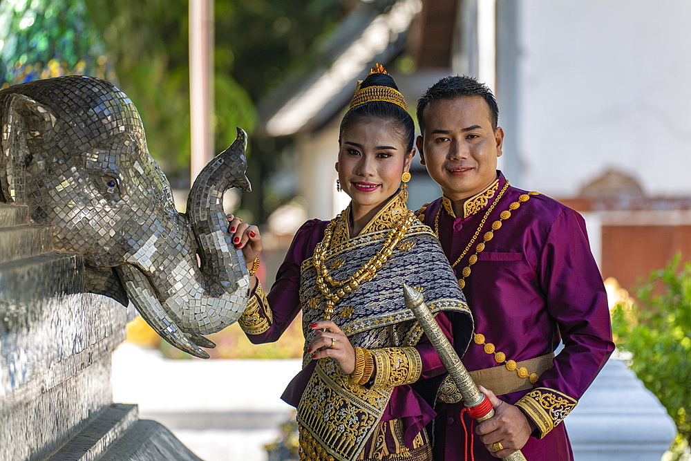 Happy wedding couple in gorgeous Laotian wedding attire during photo shoot at Wat Xieng Thong Temple, Luang Prabang, Luang Prabang Province, Laos, Asia