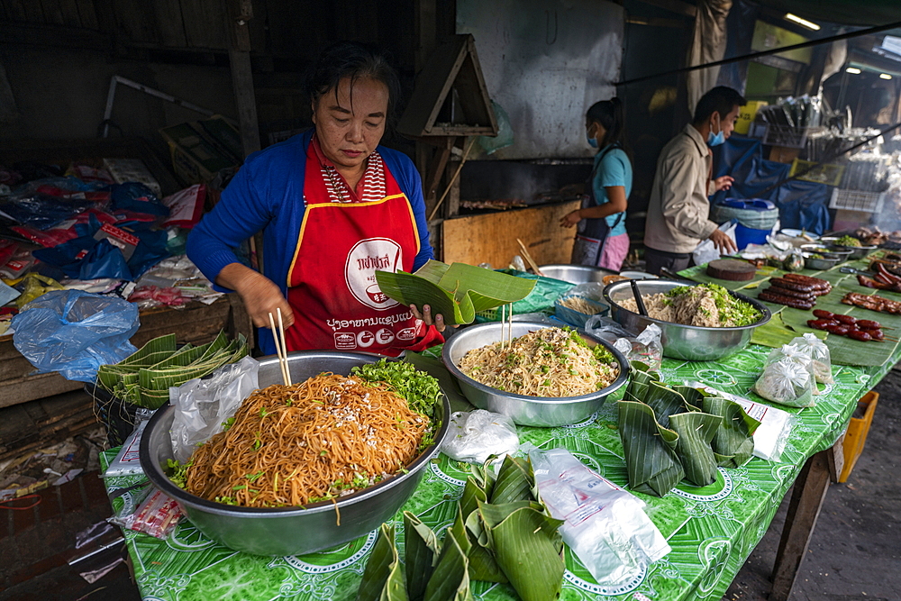 Woman prepares delicacies wrapped in banana leaves for the morning market, Luang Prabang, Luang Prabang Province, Laos, Asia