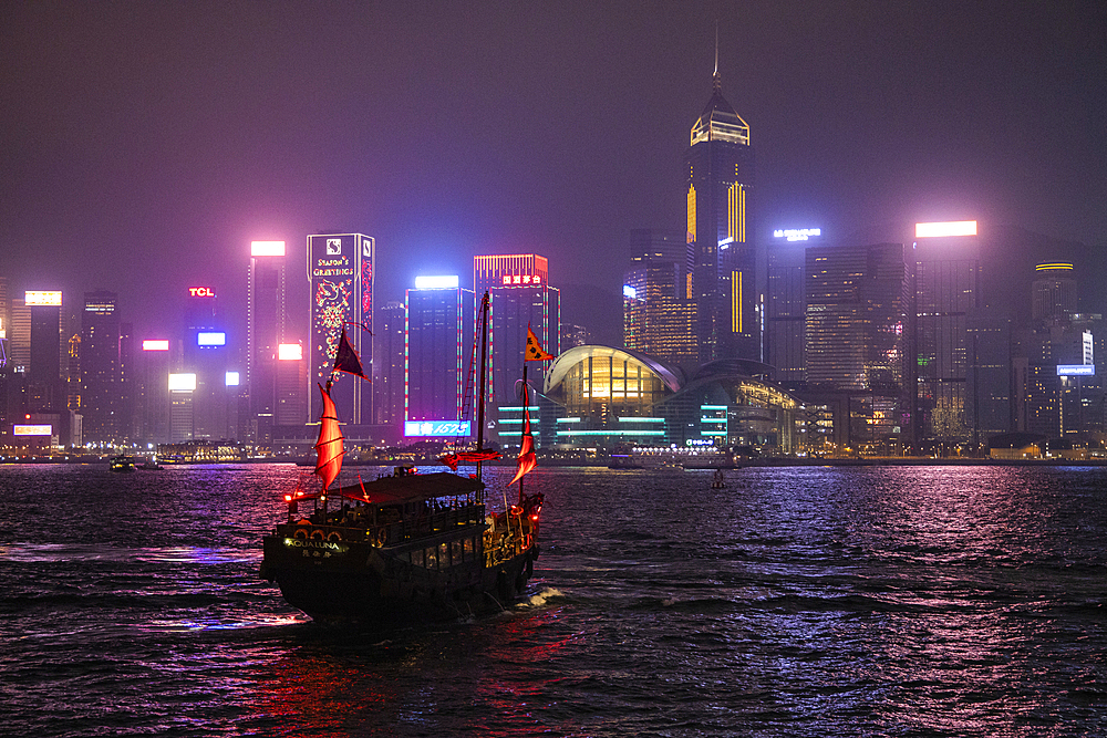 Traditional junk which serves as a tourist sightseeing boat in Victoria Harbor with Hong Kong skyline behind it at night, Hong Kong, Hong Kong, China, Asia