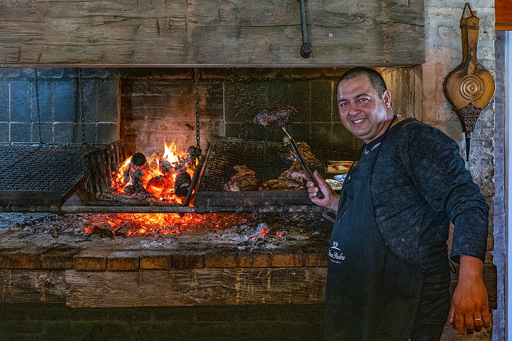 Friendly cook prepares delicious asado meat on charcoal grill in Finca Piedra, San José de Mayo, Colonia Department, Uruguay, South America