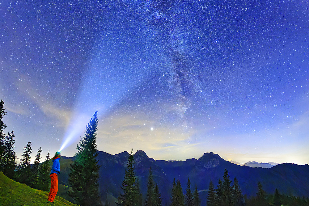 Woman stands at Farrenpoint and shines with lamp on starry sky with Milky Way, Farrenpoint, Mangfall Mountains, Bavarian Alps, Upper Bavaria, Bavaria, Germany