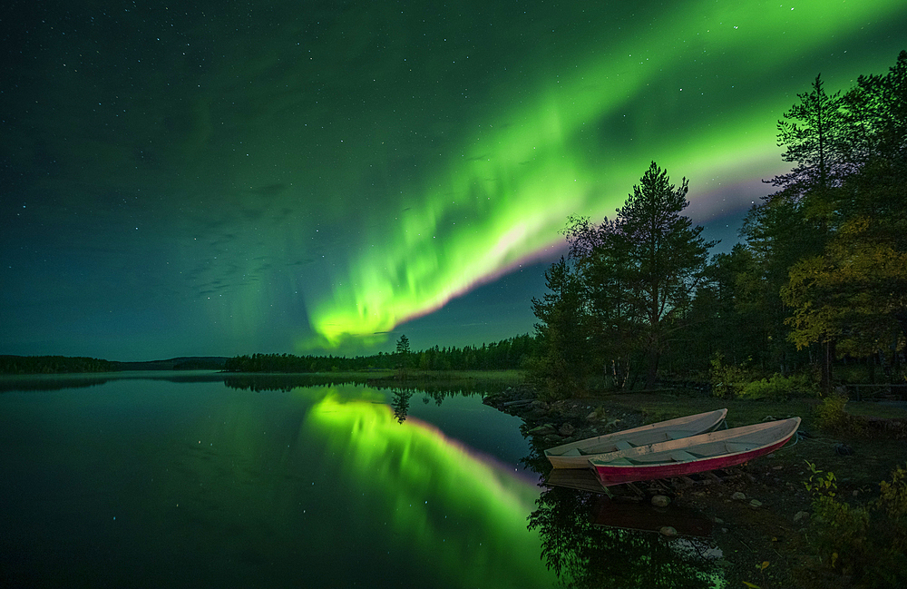 Northern lights in the night sky on the lake shore with boats in Lapland, Sweden