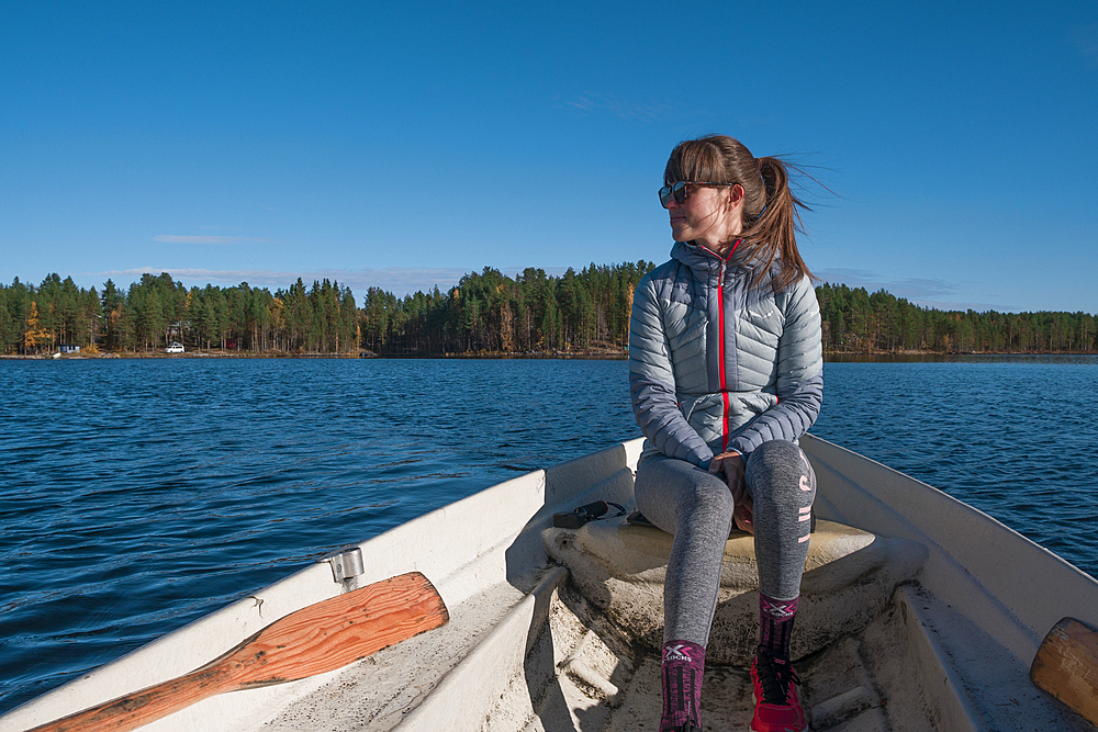 Woman sitting in paddle boat on lake in Lapland with sun and blue sky