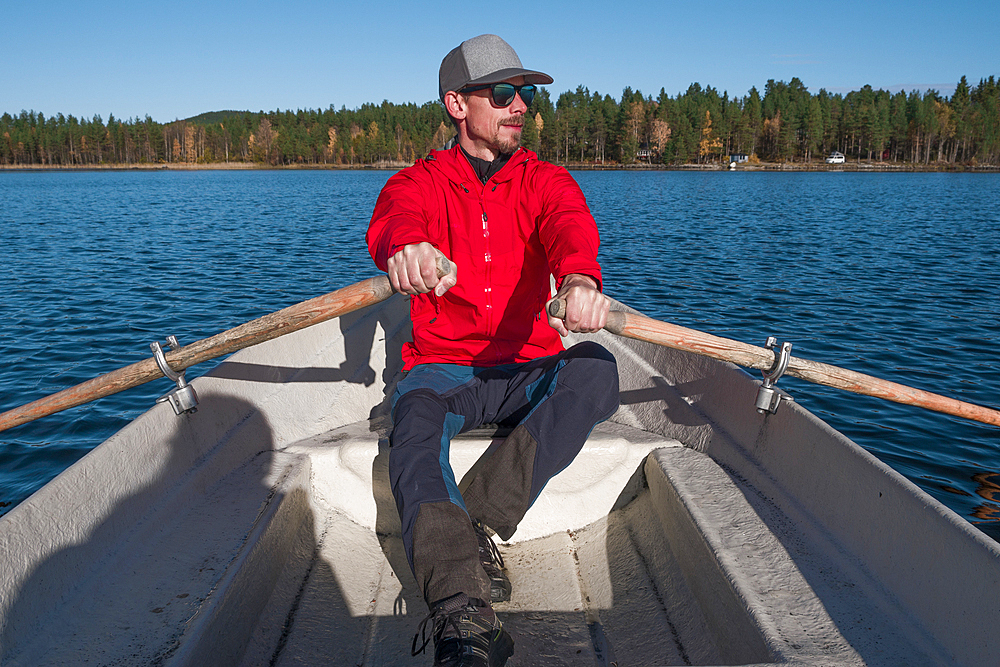 Man rowing in paddle boat on lake in Lapland with sun and blue sky