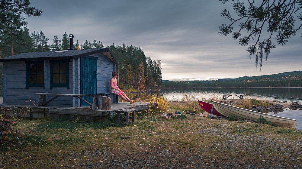 Woman sitting in front of sauna by the lake in Lapland, Sweden