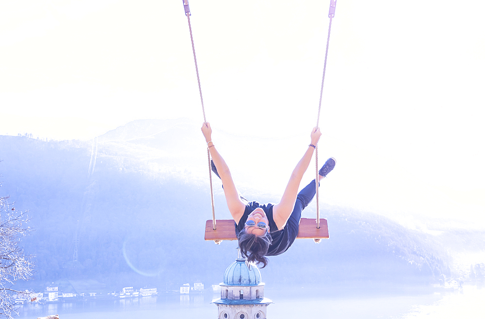 Woman on a Swing with Mountain View and Sunlight over Lake Lugano in Morcote, Ticino in Switzerland.