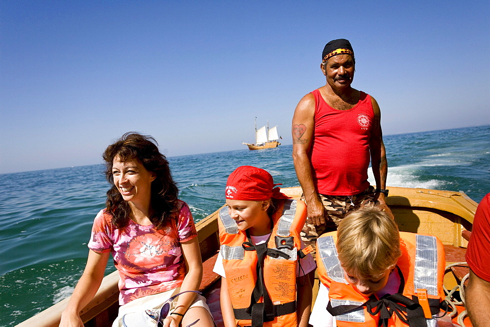 Tourists in a rubber dinghy, mother with two children, sailing boat Santa Bernada in the background, taking tourists along the steep coast of the Algarve, Portimao, Algarve, Portugal