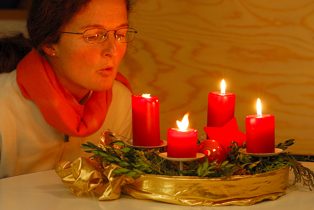 Woman blowing out four candles at advent wreath