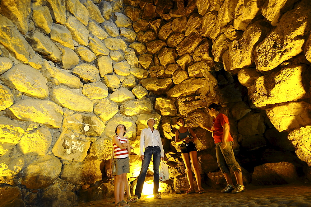 Tourists inside the illuminated Nuraghe Su Nuraxi at street of Nuraghi, South Sardinia, Italy, Europe