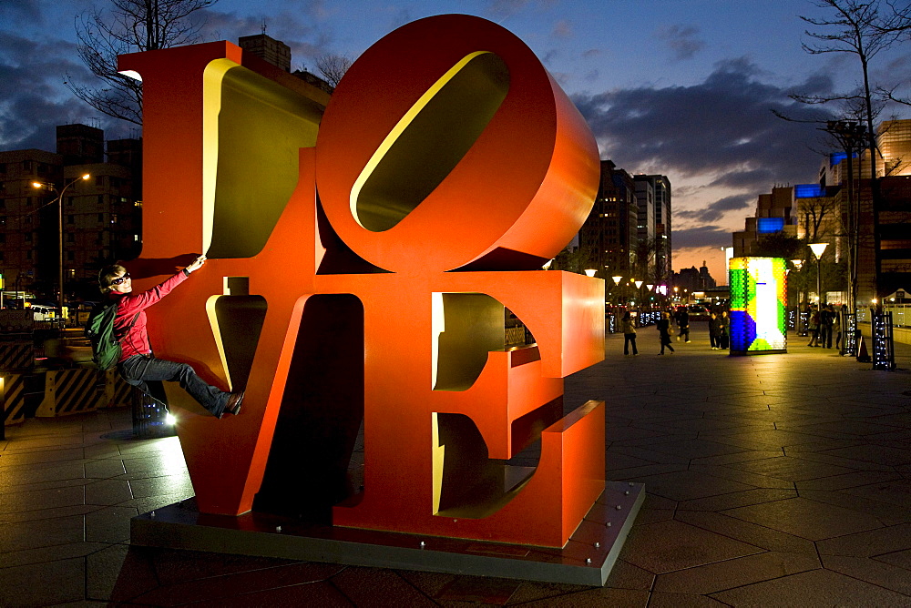 LOVE art installation in front of skyscraper Taipei 101, young German woman climbing on huge letters, Taipei, Republic of China, Taiwan, Asia