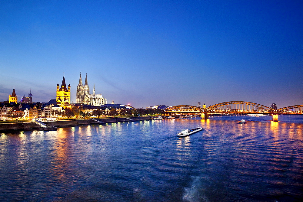 View over river Rhine to old town with cathedral and Great St. Martin church at night, Cologne, North Rhine-Westphalia, Germany