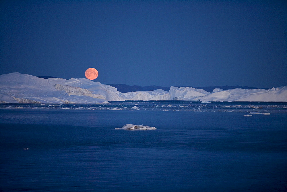 Full moon rising over icebergs from Ilulissat Kangerlua Icefjord at dusk, Ilulissat (Jakobshavn), Disko Bay, Kitaa, Greenland