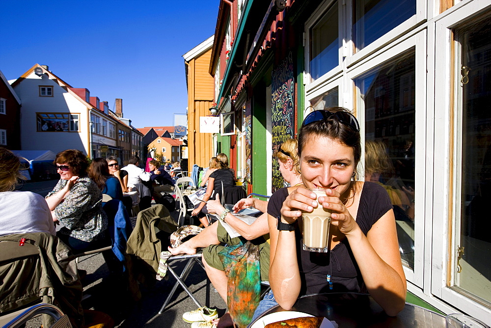 Young woman sitting in a street cafe and drinking a coffee, Mollenberg district, Trondheim, Trondelag, Norway, Scandinavia, Europe