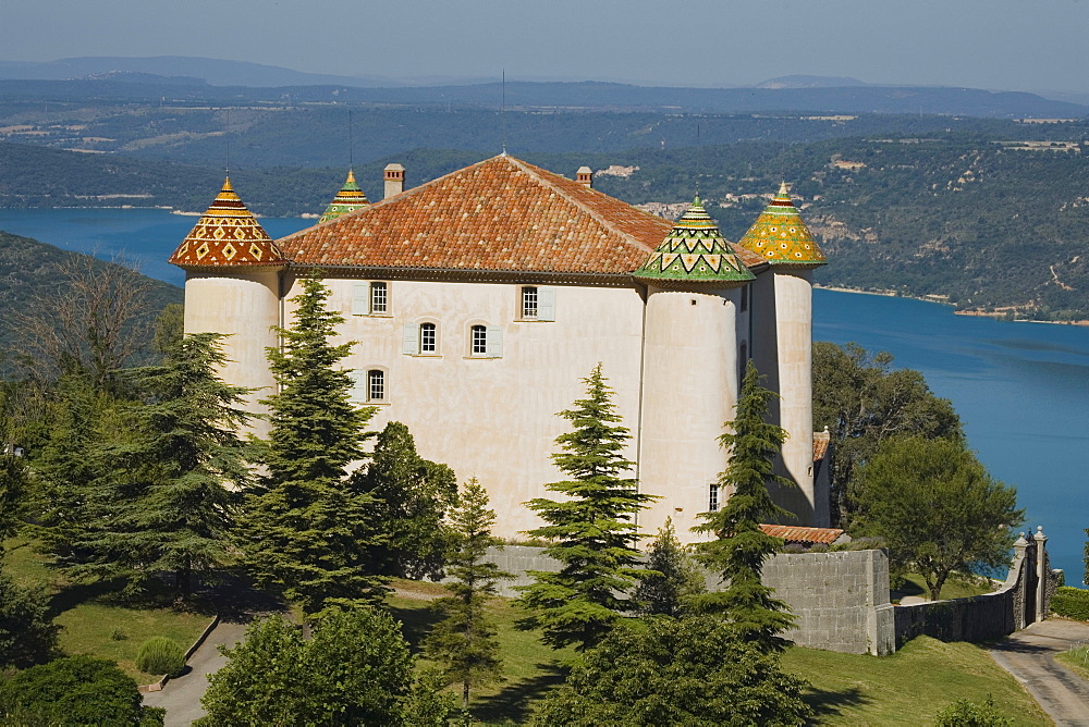 The castle of Aiguines with its coloured roof tiles in front of the lake Lac de Ste. Croix, Var, Provence, France