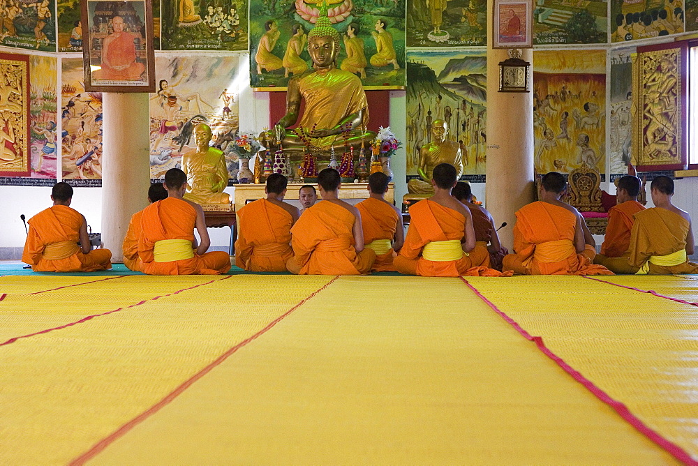 Buddhistic monks sitting in front of a Buddha statue at the monastery Vat Pa Phonphao, Luang Prabang, Laos