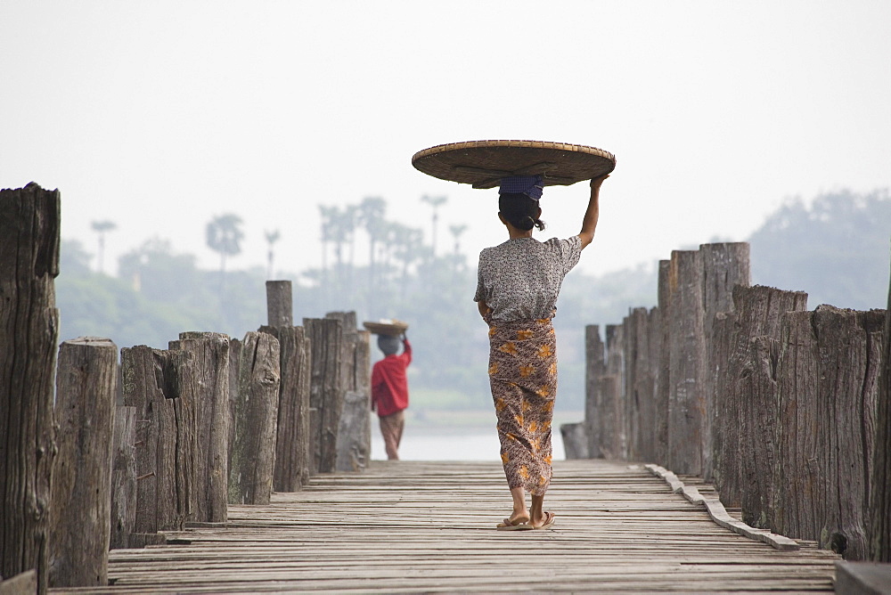 Two Burmese women, seen from behind carrying a basket on their head while walking on the U Beins Bridge in Amarapura near Mandalay, Myanmar, Burma