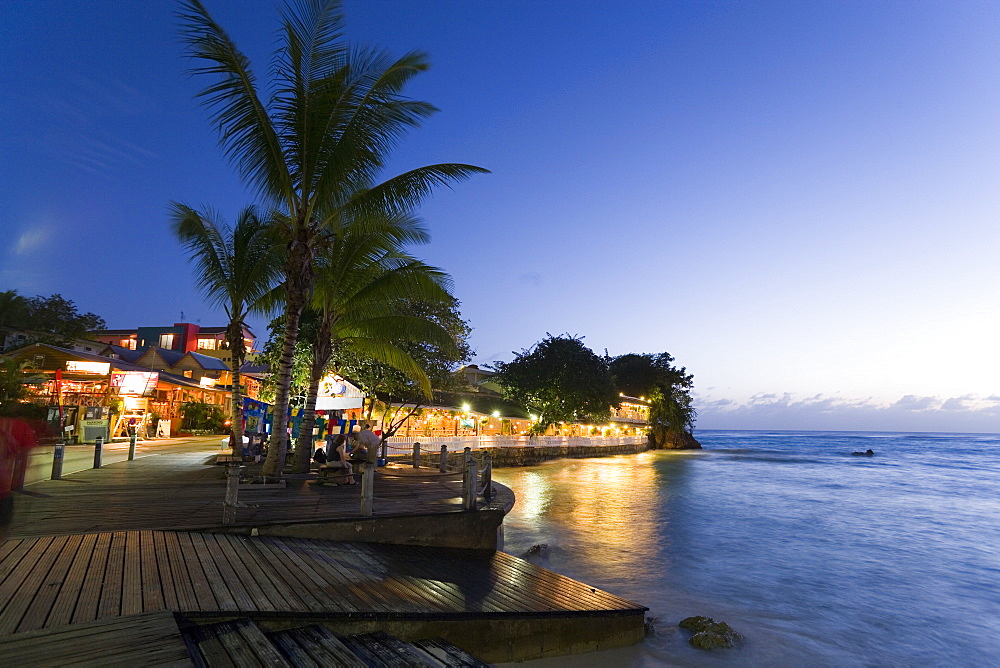 Tourists at promenade next to Pisces Restaurant at night, St. Lawrence Gap, Barbados, Caribbean