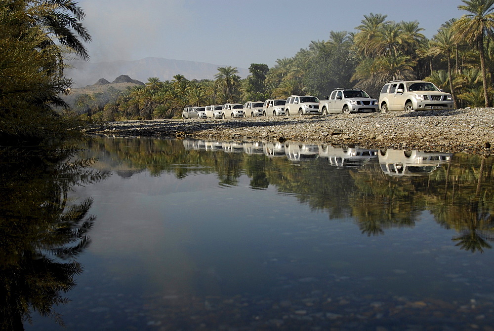 A row of all-terrain vehicles driving along a river, Al Hajar mountains, Wadi, Oman, Asia