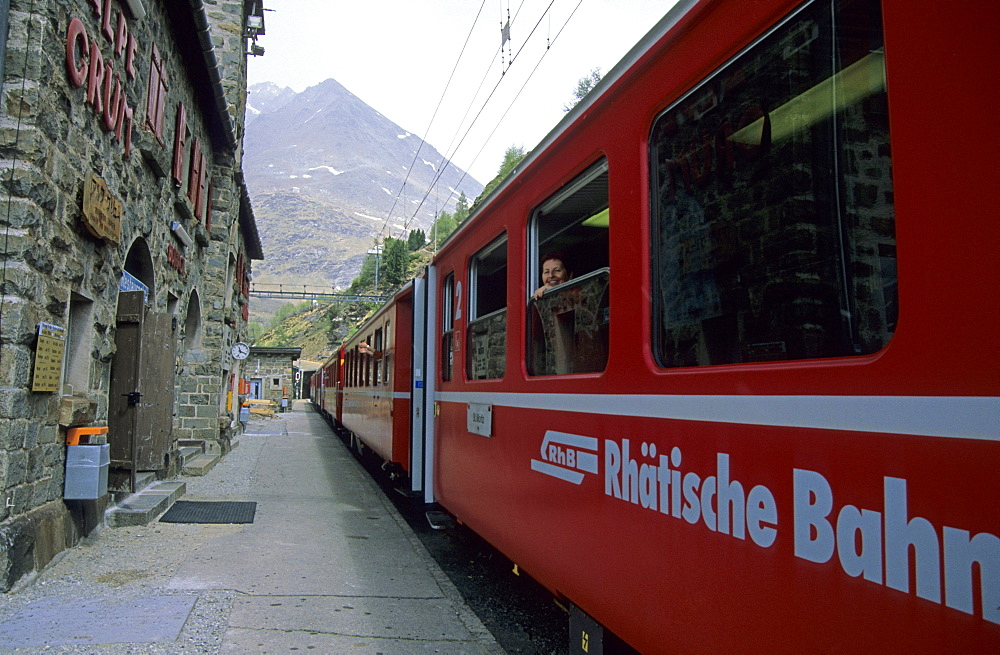 Woman smiling out of window of red train of Rhaetische Bahn at station Alpe Gruem, Alp Gruem, Ferrovia Raetia, Bernina range, Bernina, Puschlav, Grisons, Switzerland