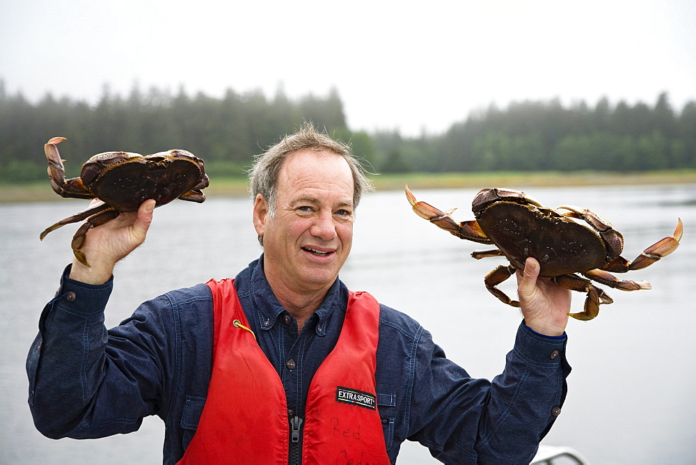 Mature man showing two crabs, Inside Passage, Southeast Alaska, USA