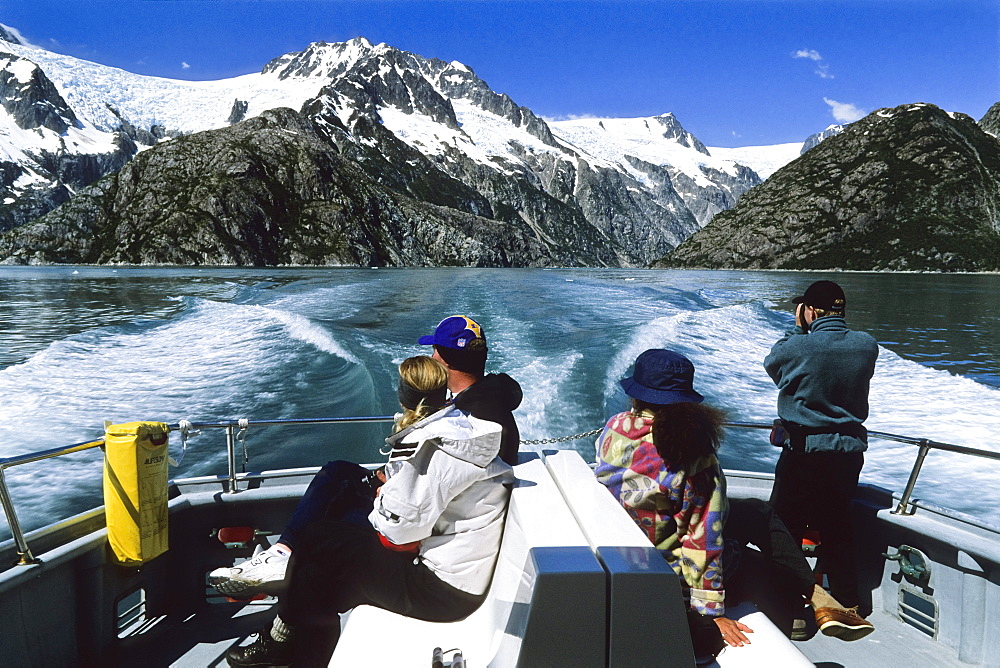 People sitting in the stern of an excursion boat, view at snow covered mountains, Inside Passage, Southeast Alaska, USA