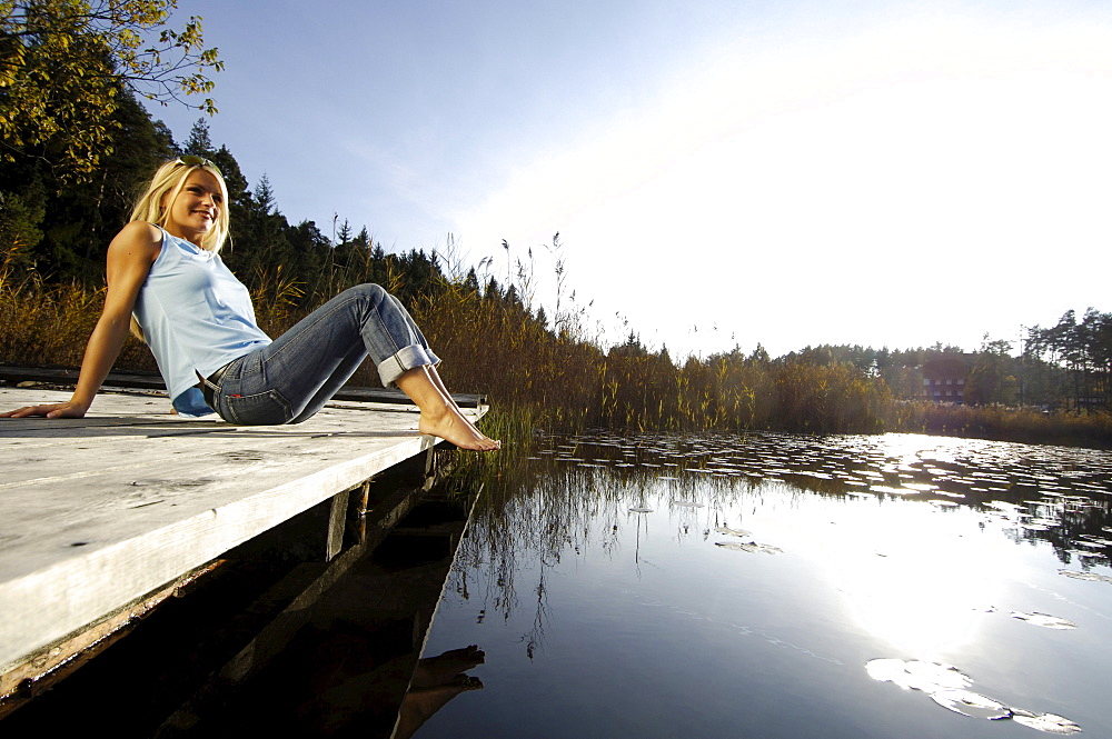 Young woman sunbathing on a jetty at a mountain lake, Voels am Schlern, South Tyrol, Italy, Europe