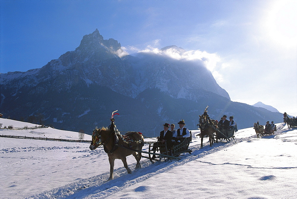 People wearing traditional costumes driving in sleighs through sunlit winter landscape, Sciliar, South Tyrol, Italy, Europe