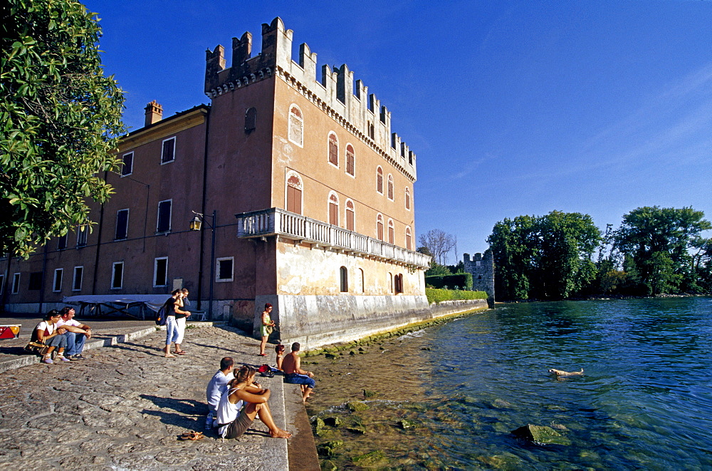 People sitting at the lakeside at the Scaliger castle, Lazise, Lake Garda, Veneto, Italy, Europe