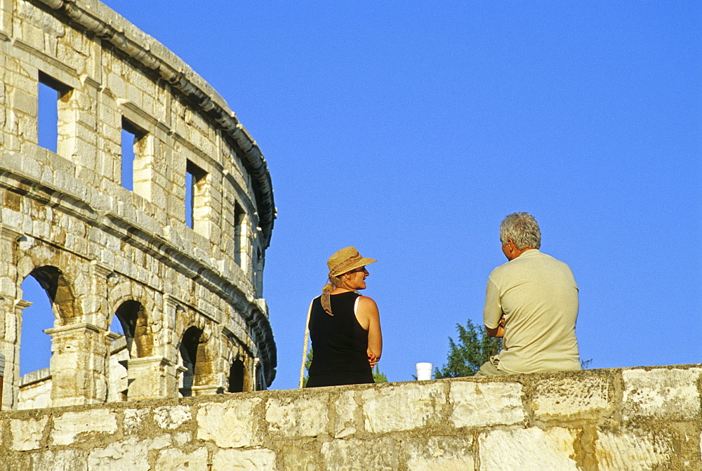 Couple on the city wall in front of the Roman amphitheater under blue sky, Pula, Croatian Adriatic Sea, Istria, Croatia, Europe