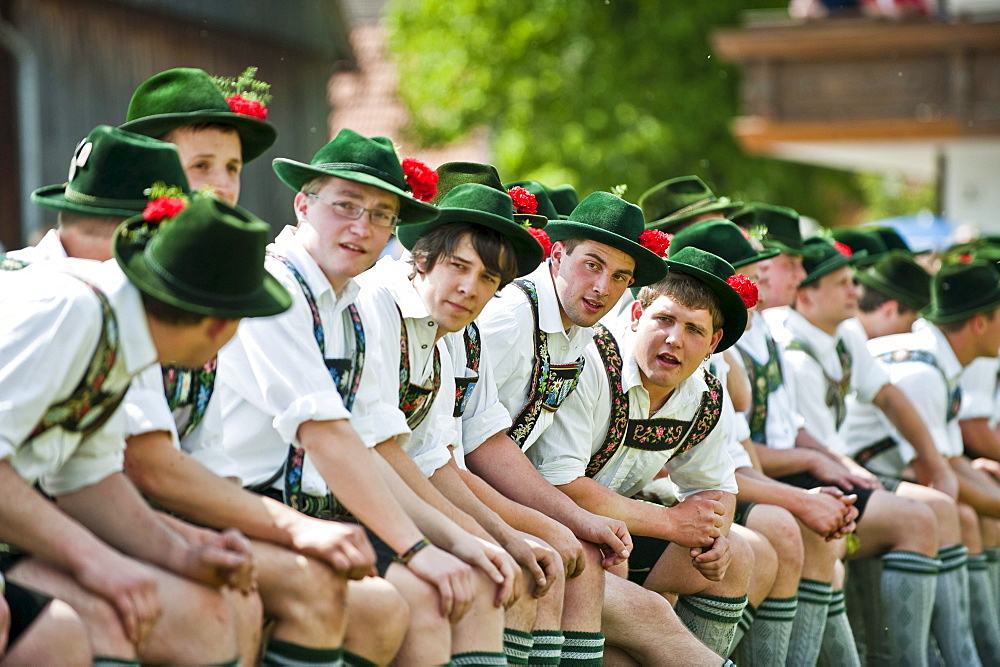 Young men wearing traditional costumes sitting side by side, May Running, Antdorf, Upper Bavaria, Germany