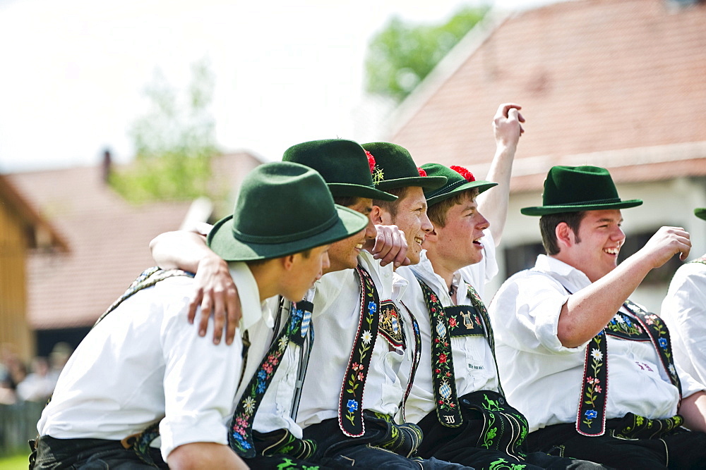 Young men wearing traditional costumes sitting side by side, May Running, Antdorf, Upper Bavaria, Germany