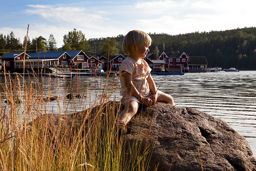 A little girl sitting on a rock, in the background the village Norrfaellsviken, Hoega Kusten, Sweden, Europe