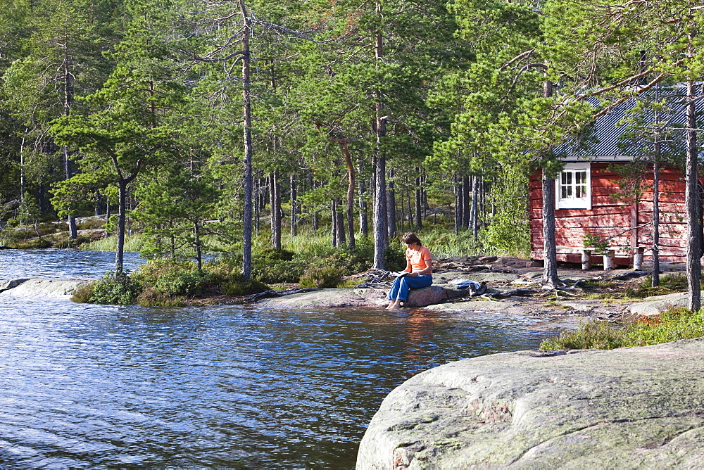 Woman sitting in front of a small cottage at the lake Taernaettvatten, national park Skuleskogen, Hoega Kusten, Vaesternorrland, Sweden, Europe