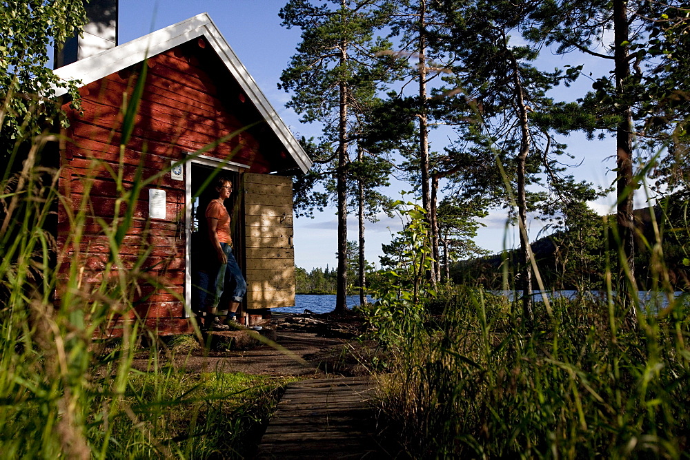 Woman and small cottage at the lake Taernaettvatten, nationalpark Skuleskogen, Hoega Kusten, Vaesternorrland, Sweden, Europe